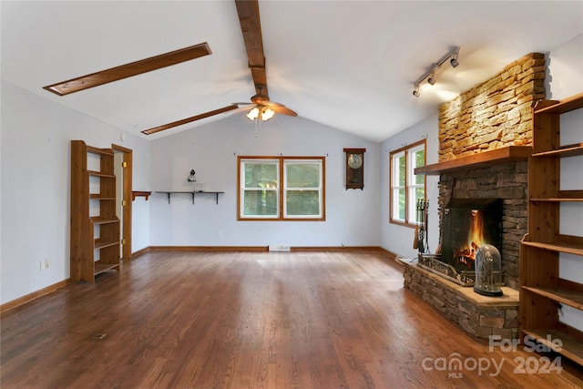 unfurnished living room with dark hardwood / wood-style floors, a stone fireplace, rail lighting, ceiling fan, and vaulted ceiling with beams