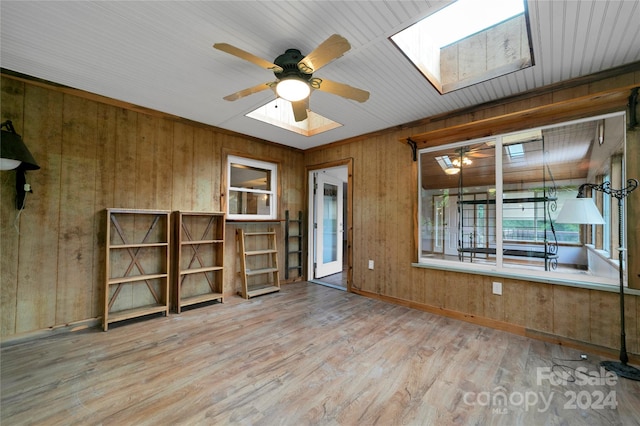 spare room featuring a skylight, hardwood / wood-style floors, ceiling fan, and wooden walls