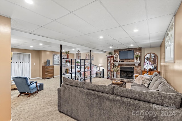 carpeted living room featuring a drop ceiling and a stone fireplace