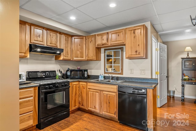 kitchen with black appliances, hardwood / wood-style flooring, sink, and a drop ceiling