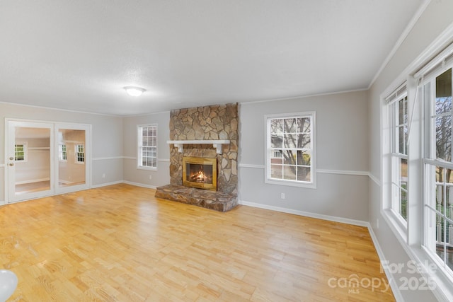 unfurnished living room featuring a stone fireplace, a wealth of natural light, and light hardwood / wood-style floors