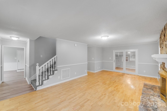 unfurnished living room with crown molding, light hardwood / wood-style floors, a textured ceiling, and a multi sided fireplace