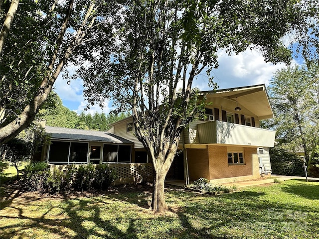 view of front of property featuring brick siding, a front lawn, a balcony, and a sunroom