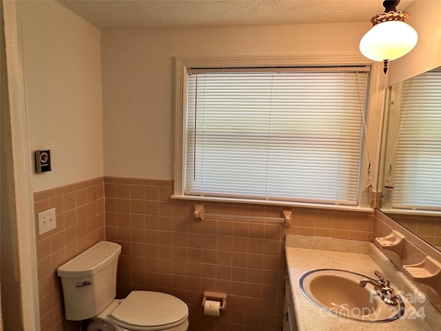 bathroom with a textured ceiling, vanity, tasteful backsplash, tile walls, and toilet