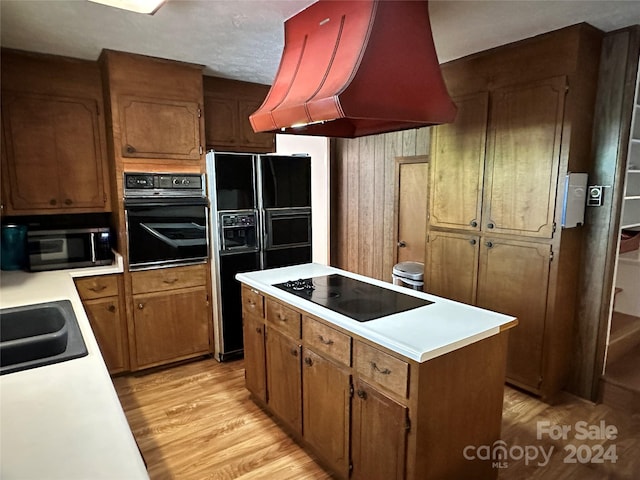 kitchen with black appliances, premium range hood, a center island, sink, and light wood-type flooring