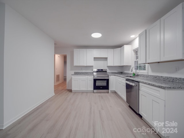 kitchen featuring stainless steel appliances, light stone counters, light wood-type flooring, and white cabinets