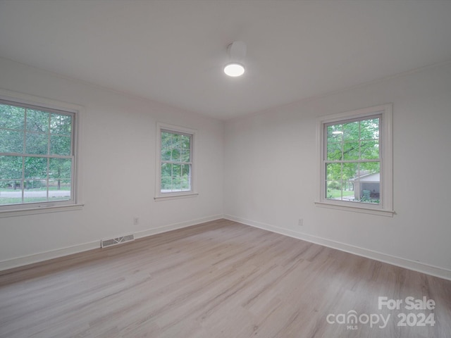 empty room featuring visible vents, light wood-style floors, baseboards, and a wealth of natural light