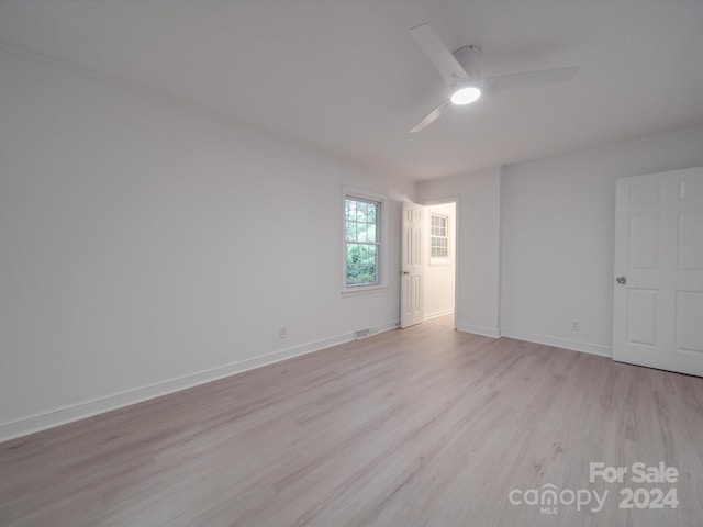 spare room featuring light wood finished floors, a ceiling fan, and baseboards