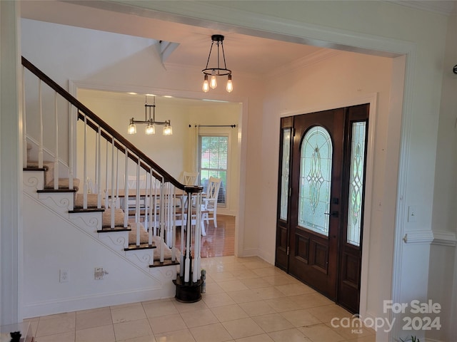 tiled foyer featuring an inviting chandelier and crown molding