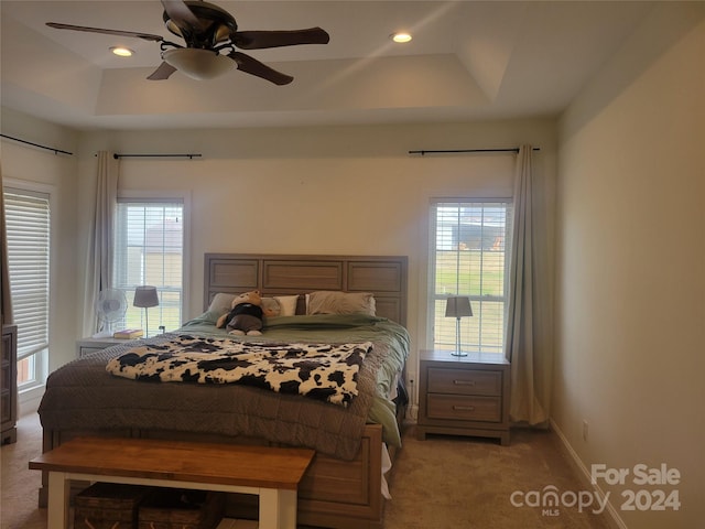 carpeted bedroom with multiple windows, a tray ceiling, and ceiling fan