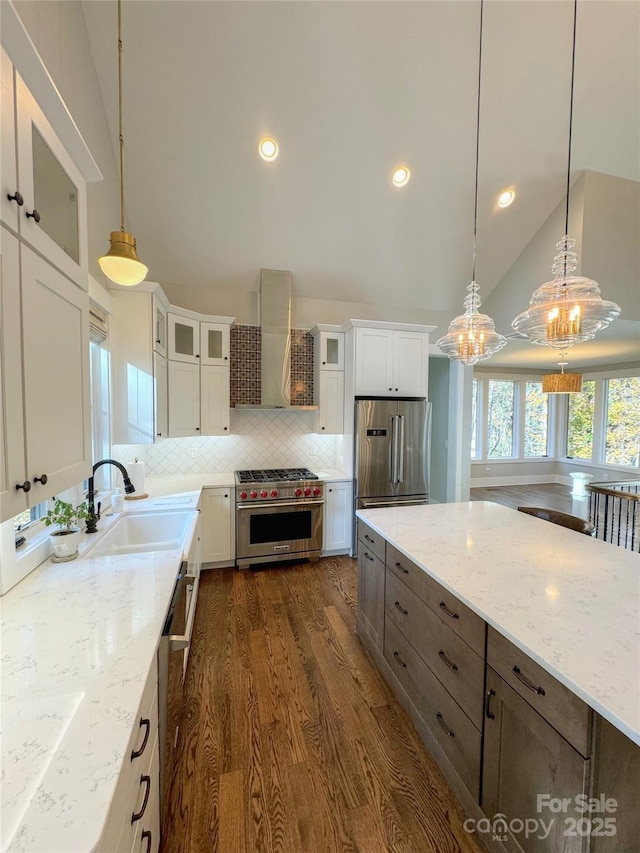 kitchen featuring dark wood finished floors, wall chimney exhaust hood, light stone countertops, stainless steel appliances, and white cabinetry