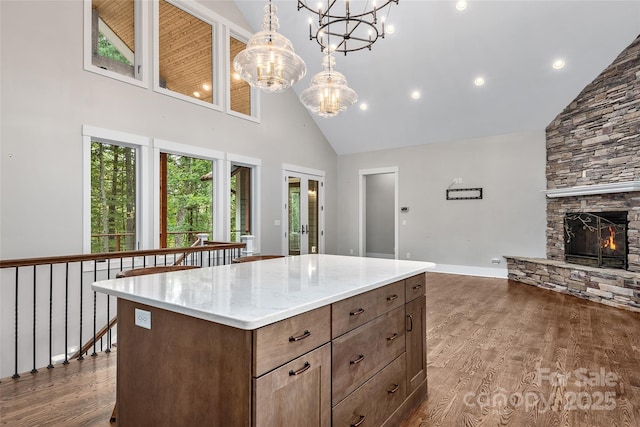 kitchen with high vaulted ceiling, a stone fireplace, dark wood-style flooring, a center island, and decorative light fixtures