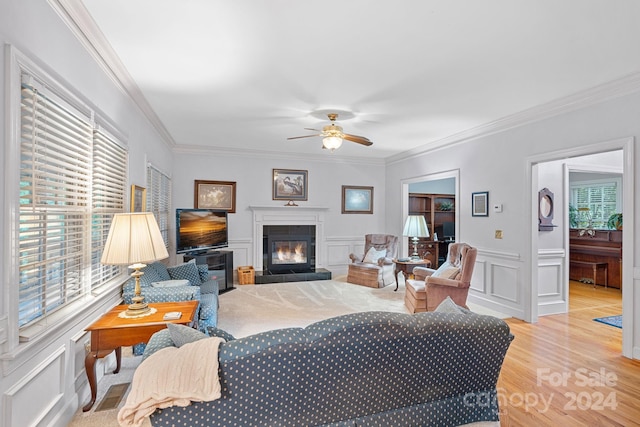 living room with light hardwood / wood-style floors, ceiling fan, ornamental molding, and a fireplace