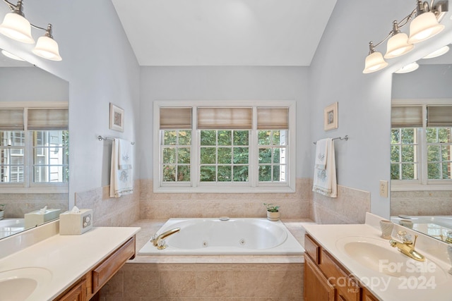 bathroom featuring a healthy amount of sunlight, vanity, a relaxing tiled tub, and vaulted ceiling