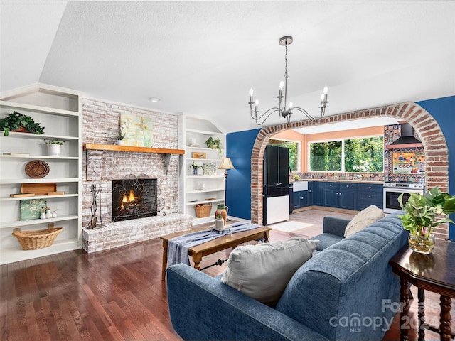 living room featuring an inviting chandelier, a brick fireplace, dark hardwood / wood-style flooring, lofted ceiling, and a textured ceiling