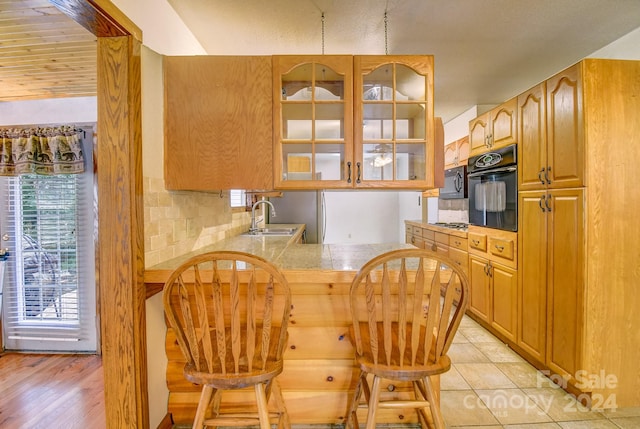 kitchen featuring backsplash, kitchen peninsula, sink, black oven, and light wood-type flooring