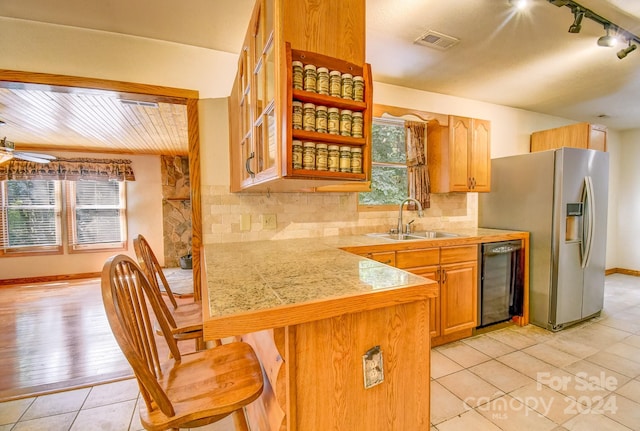 kitchen featuring sink, stainless steel fridge, ceiling fan, a kitchen bar, and decorative backsplash