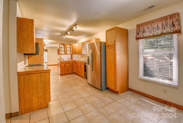 kitchen with tasteful backsplash, rail lighting, light tile patterned floors, sink, and appliances with stainless steel finishes