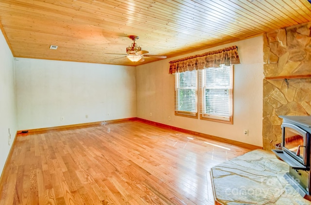 unfurnished living room with a wood stove, ceiling fan, a stone fireplace, and wood ceiling