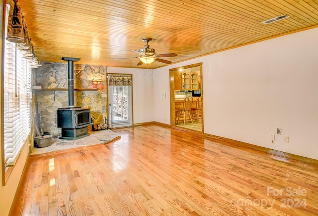 unfurnished living room with light wood-type flooring, ornamental molding, a wood stove, ceiling fan, and wooden ceiling