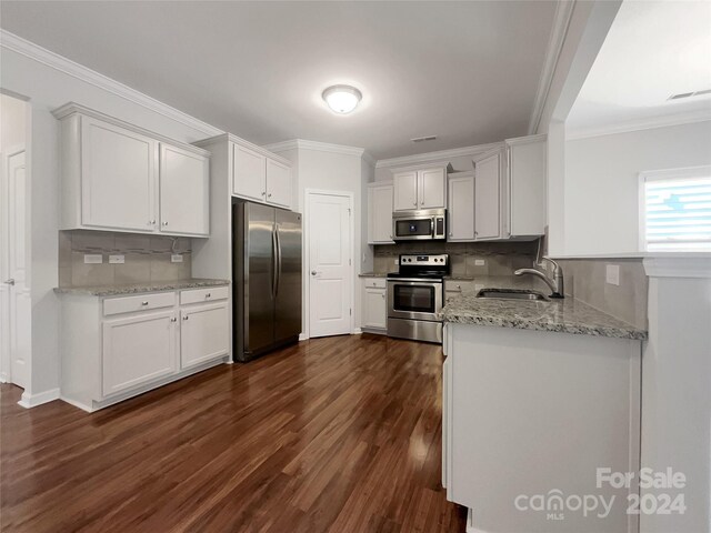 kitchen with dark hardwood / wood-style flooring, crown molding, stainless steel appliances, white cabinetry, and light stone counters