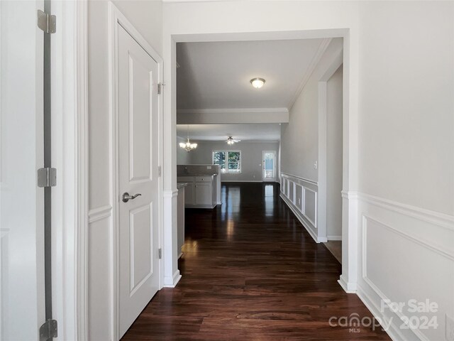 hallway with ornamental molding, dark hardwood / wood-style floors, and a chandelier