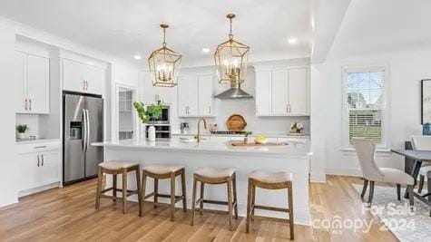 kitchen featuring appliances with stainless steel finishes, white cabinets, a kitchen island with sink, and light hardwood / wood-style floors