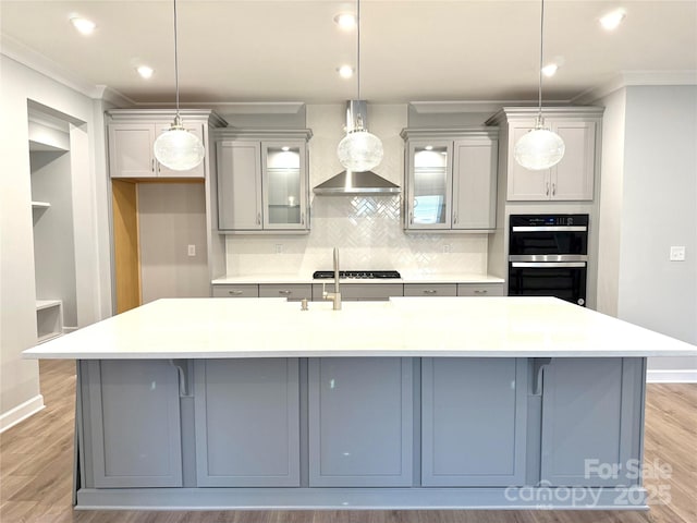 kitchen with light wood-type flooring, tasteful backsplash, gray cabinetry, and a large island with sink