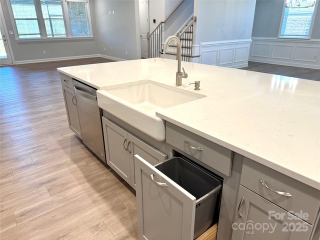 kitchen with light wood-style flooring, dishwasher, gray cabinetry, and a sink