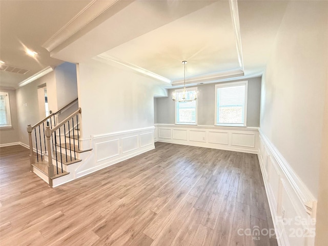 unfurnished dining area featuring stairway, wood finished floors, visible vents, a tray ceiling, and ornamental molding