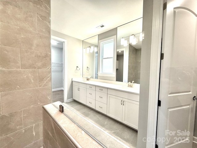 full bathroom featuring double vanity, a spacious closet, visible vents, and a sink