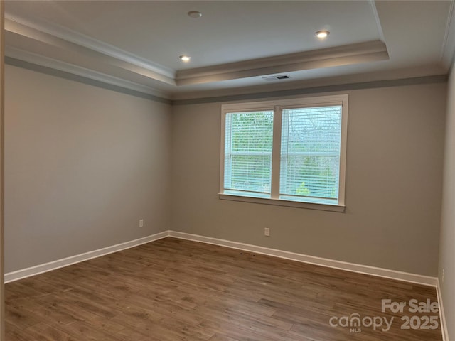 spare room featuring visible vents, ornamental molding, wood finished floors, baseboards, and a raised ceiling