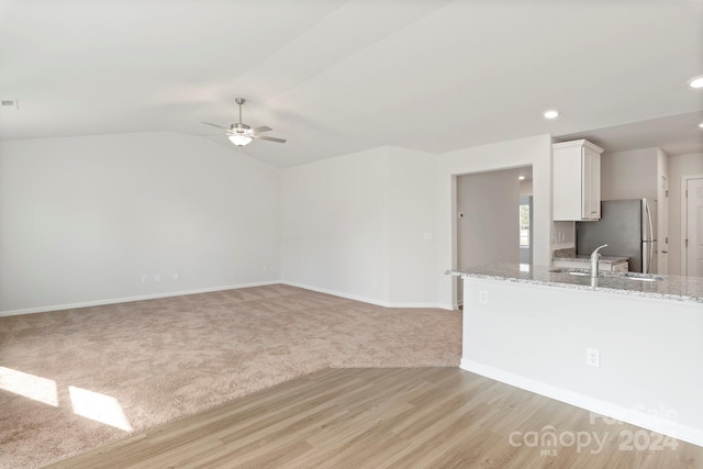 unfurnished living room with light hardwood / wood-style floors, ceiling fan, lofted ceiling, and sink