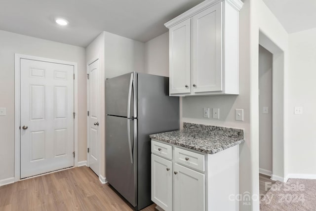 kitchen featuring baseboards, light wood-style floors, white cabinets, freestanding refrigerator, and light stone countertops