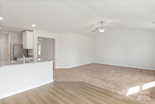 unfurnished living room featuring lofted ceiling, light colored carpet, ceiling fan, and sink