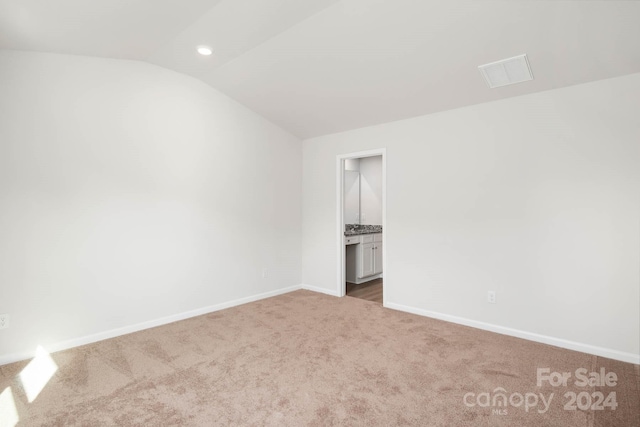 unfurnished bedroom featuring ensuite bath, vaulted ceiling, and light colored carpet