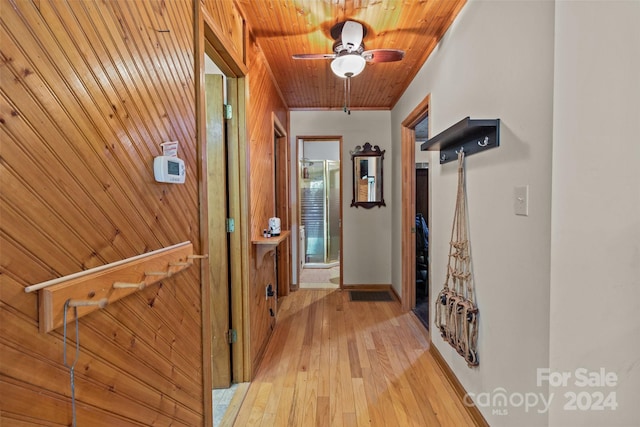 hall with wood walls, light wood-type flooring, and wooden ceiling