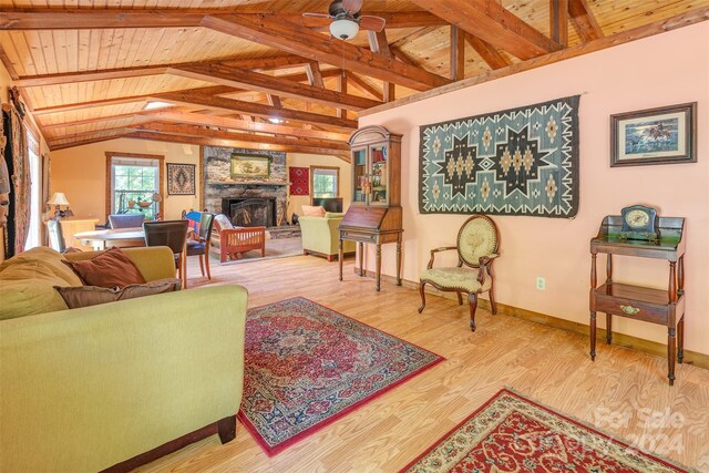 living room with light hardwood / wood-style flooring, wood ceiling, a stone fireplace, ceiling fan, and vaulted ceiling with beams