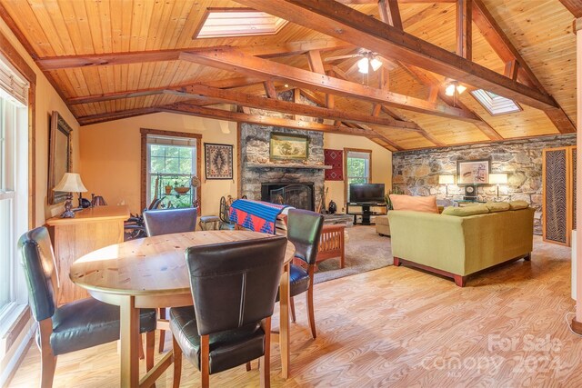 dining area with vaulted ceiling with skylight, hardwood / wood-style floors, ceiling fan, a stone fireplace, and wooden ceiling