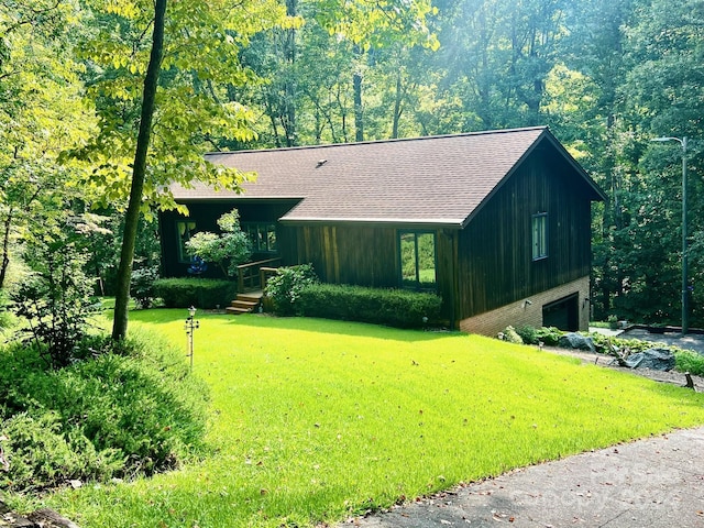 view of front of home featuring an attached garage, driveway, roof with shingles, a front yard, and a wooded view