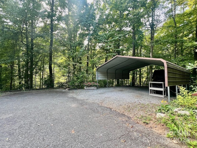 view of vehicle parking featuring driveway, a view of trees, and a detached carport