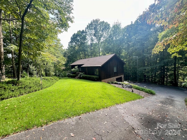 view of front facade featuring driveway, an attached garage, a wooded view, and a front yard