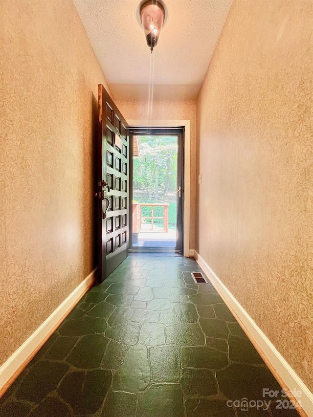 doorway with visible vents, a textured ceiling, stone tile flooring, and baseboards