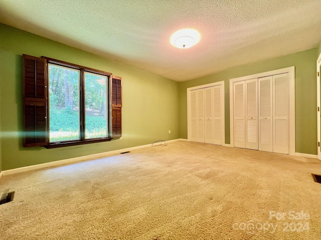 unfurnished bedroom with multiple closets, carpet flooring, a textured ceiling, and baseboards