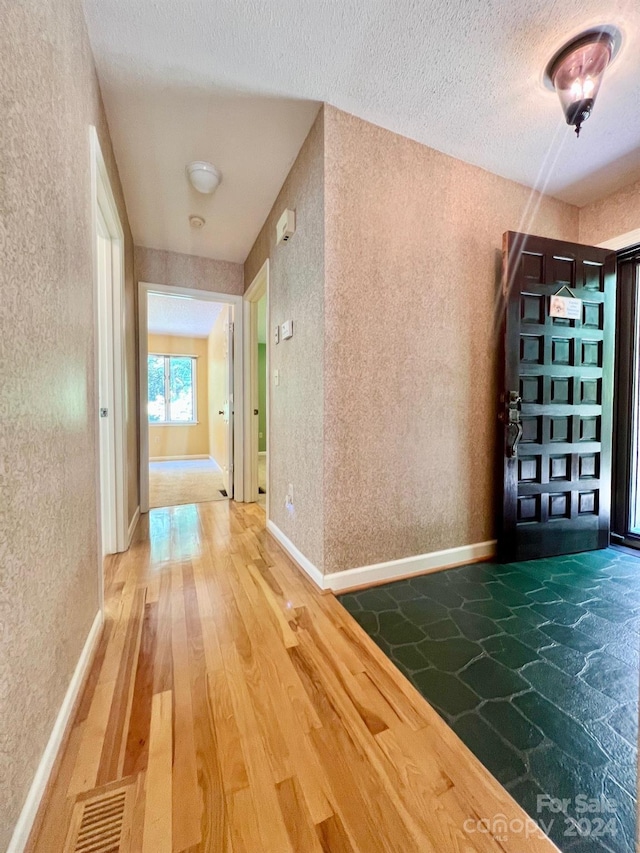 hall featuring a textured ceiling, a textured wall, wood finished floors, visible vents, and baseboards