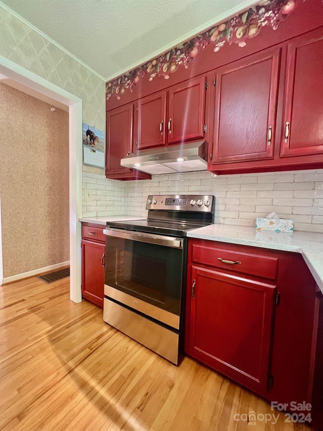 kitchen featuring under cabinet range hood, electric stove, light countertops, light wood finished floors, and wallpapered walls