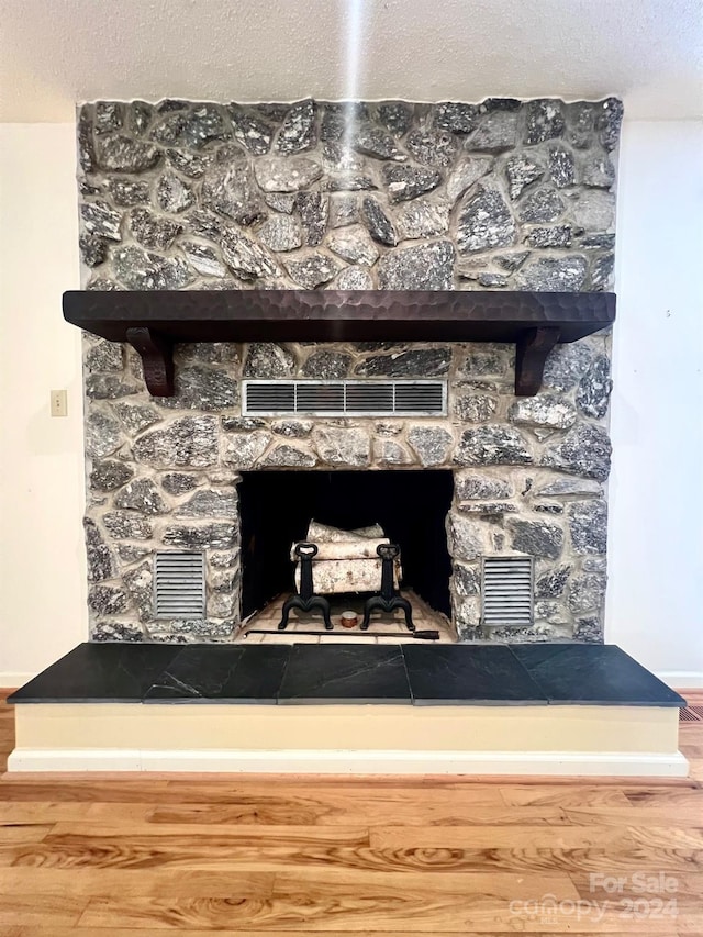 interior details with visible vents, a stone fireplace, a textured ceiling, and wood finished floors