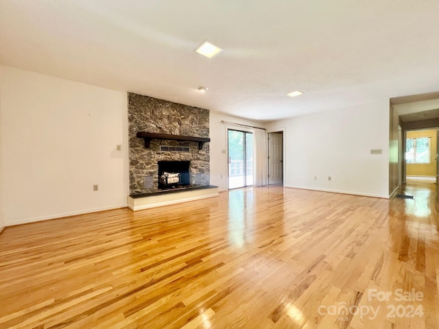 unfurnished living room featuring light wood-type flooring, a stone fireplace, and baseboards