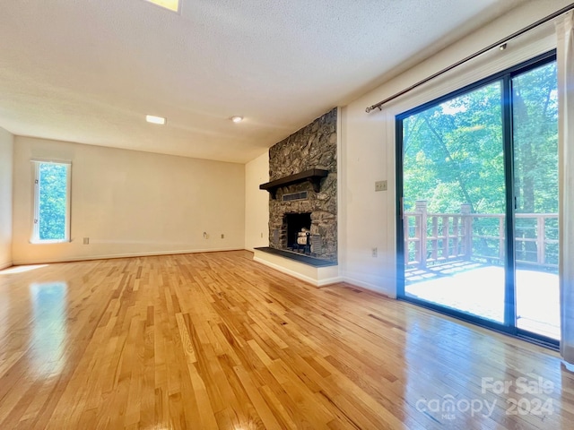 unfurnished living room featuring a textured ceiling, a stone fireplace, light wood-style flooring, and baseboards