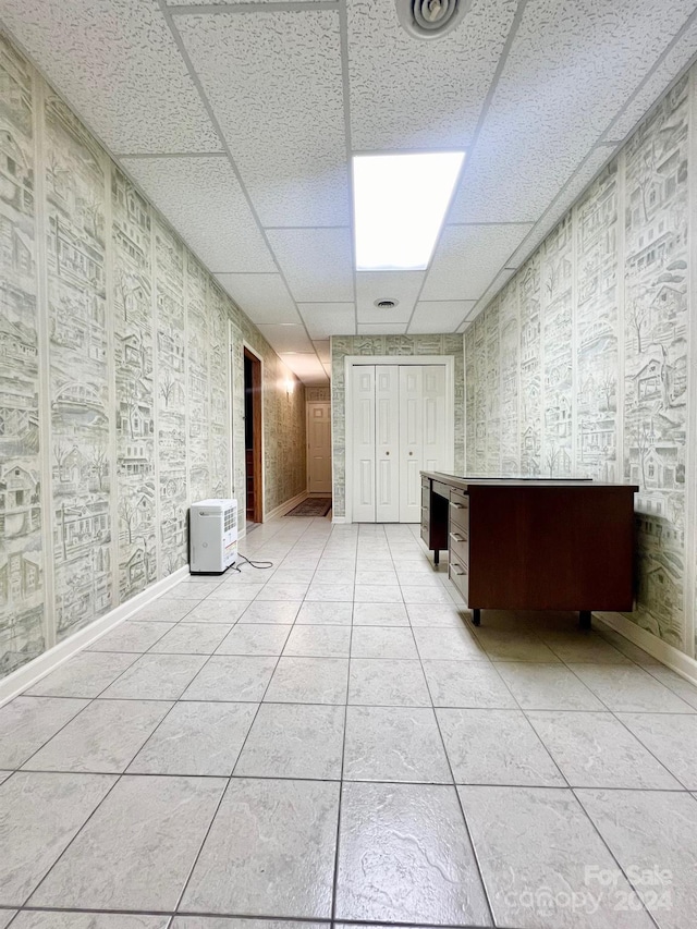 unfurnished room featuring a paneled ceiling, baseboards, and light tile patterned floors